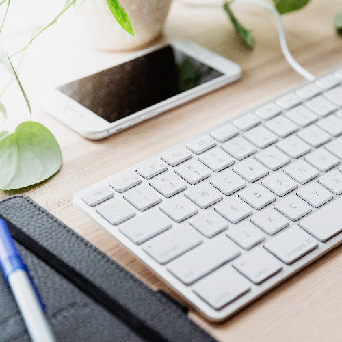 Keyboard and smartphone on a wooden desk with a plant in the background