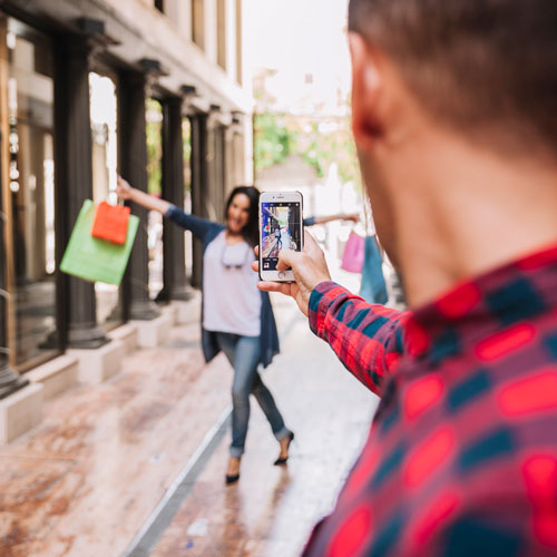 Person taking a photo of another person with a phone on a city street.
